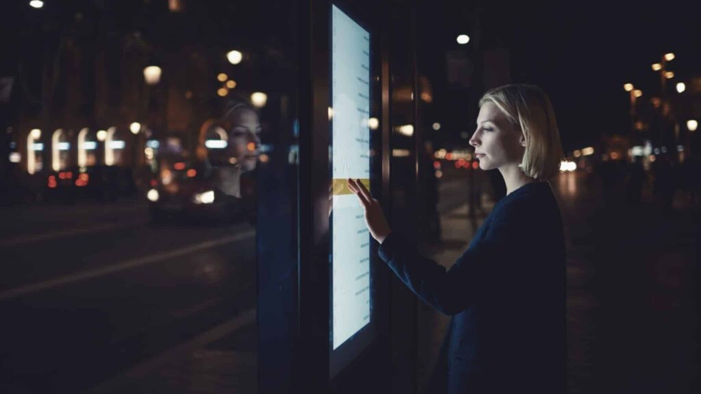 a woman using a touchscreen display in a public environment at night